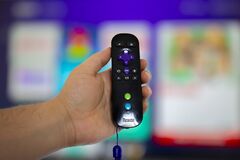 A person holding a Roku remote control with a screen tv on the background